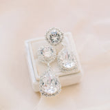 A pair of elegant teardrop crystal earrings with intricate halo detailing, perfect for a bride's wedding day look.