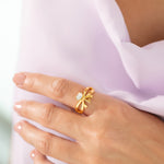 A person wearing a gold-plated, bow-shaped ring with a central crystal on their finger.
