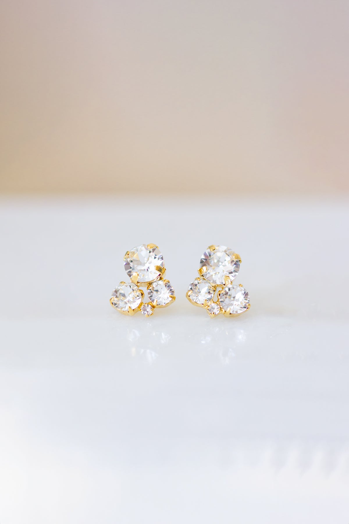A pair of gold-plated brass stud earrings with clear crystals on a white background.
