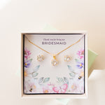 A jewelry set including a necklace and stud earrings, displayed in a box with a floral pattern and the text 'Thank you for being my Bridesmaid'. The jewelry is plated in gold, and has gold and white crystals.