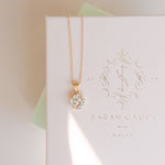 A gold-plated necklace with a crystal pendant, presented on a white box with 'SARAH GAUCI MALTA' branding.