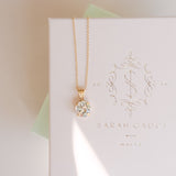 A gold-plated necklace with a crystal pendant, presented on a white box with 'SARAH GAUCI MALTA' branding.