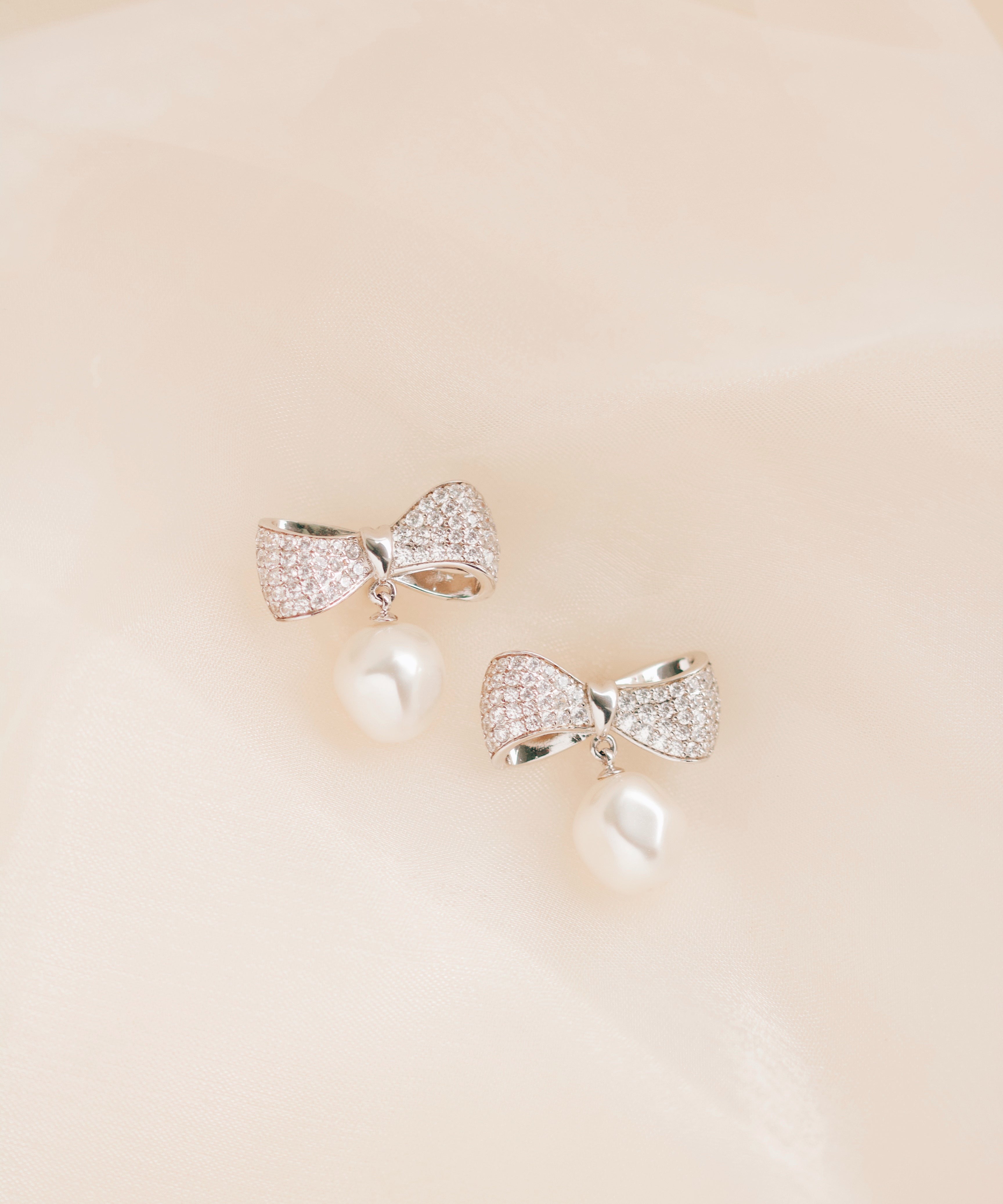 Silver bow-shaped earrings on a beige background