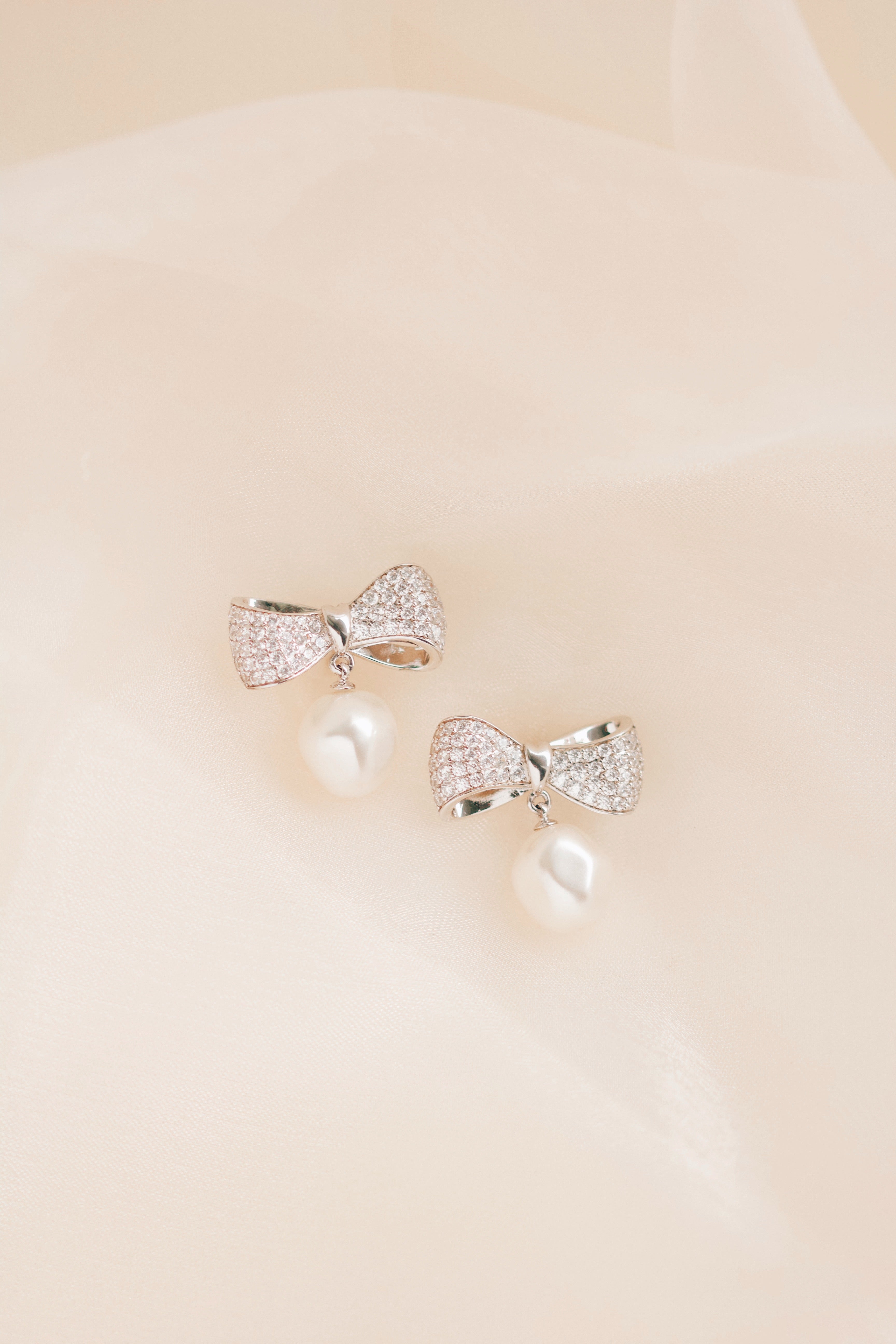 Silver bow-shaped earrings on a beige background