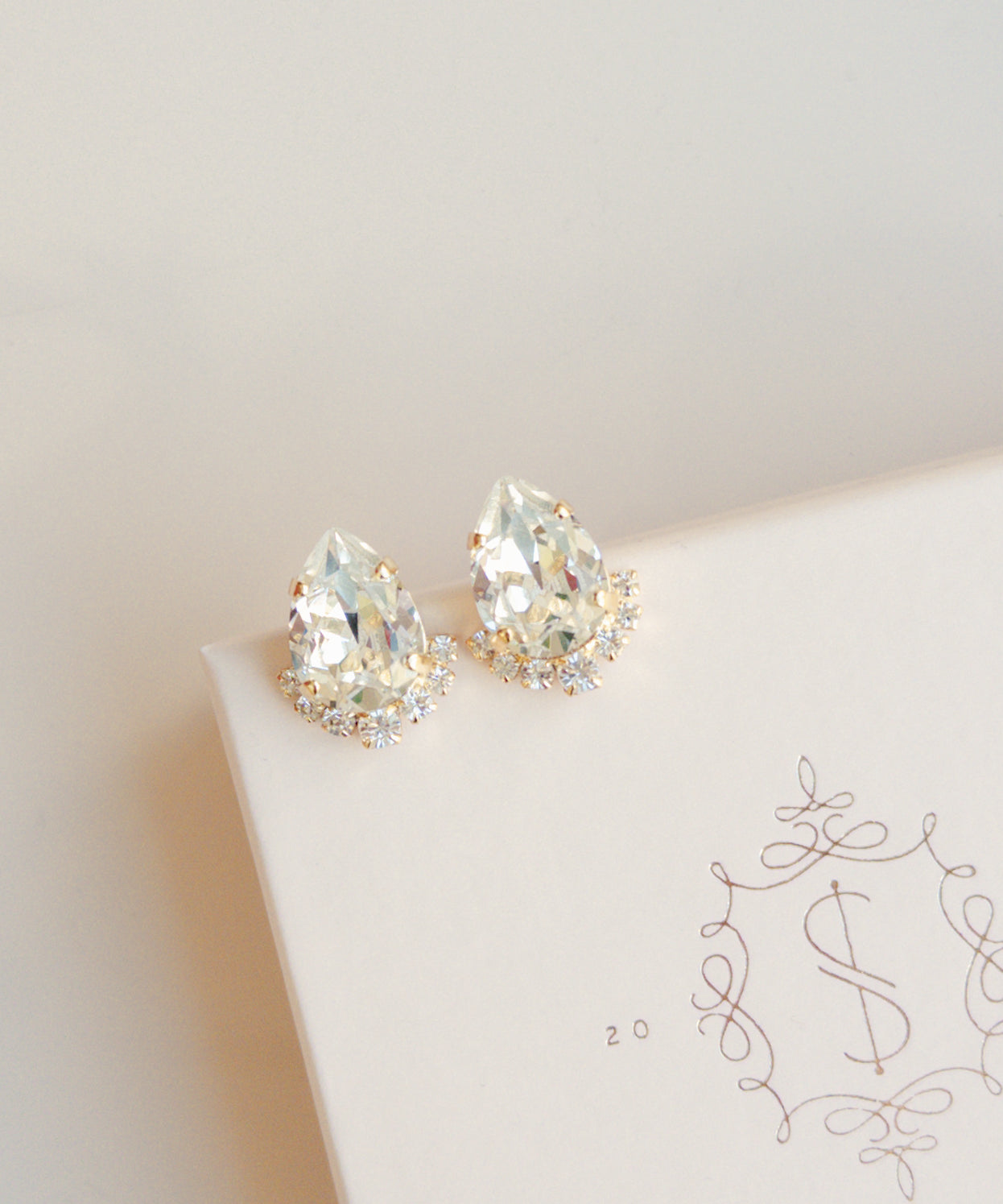 A pair of gold-colored stud earrings adorned with crystal embellishments, displayed on a white surface with a patterned design.