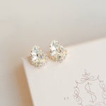 A pair of gold-colored stud earrings adorned with crystal embellishments, displayed on a white surface with a patterned design.