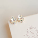 A pair of gold-colored stud earrings adorned with crystal embellishments, displayed on a white surface with a patterned design.