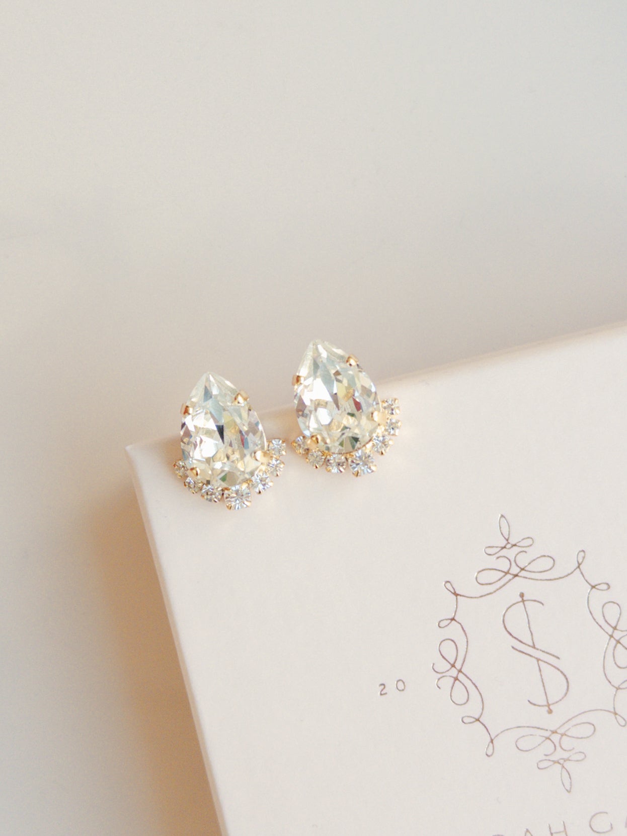 A pair of gold-colored stud earrings adorned with crystal embellishments, displayed on a white surface with a patterned design.