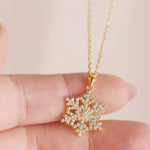 Gold snowflake pendant necklace held between fingers against a light background
