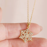 Gold snowflake pendant necklace held between fingers against a light background