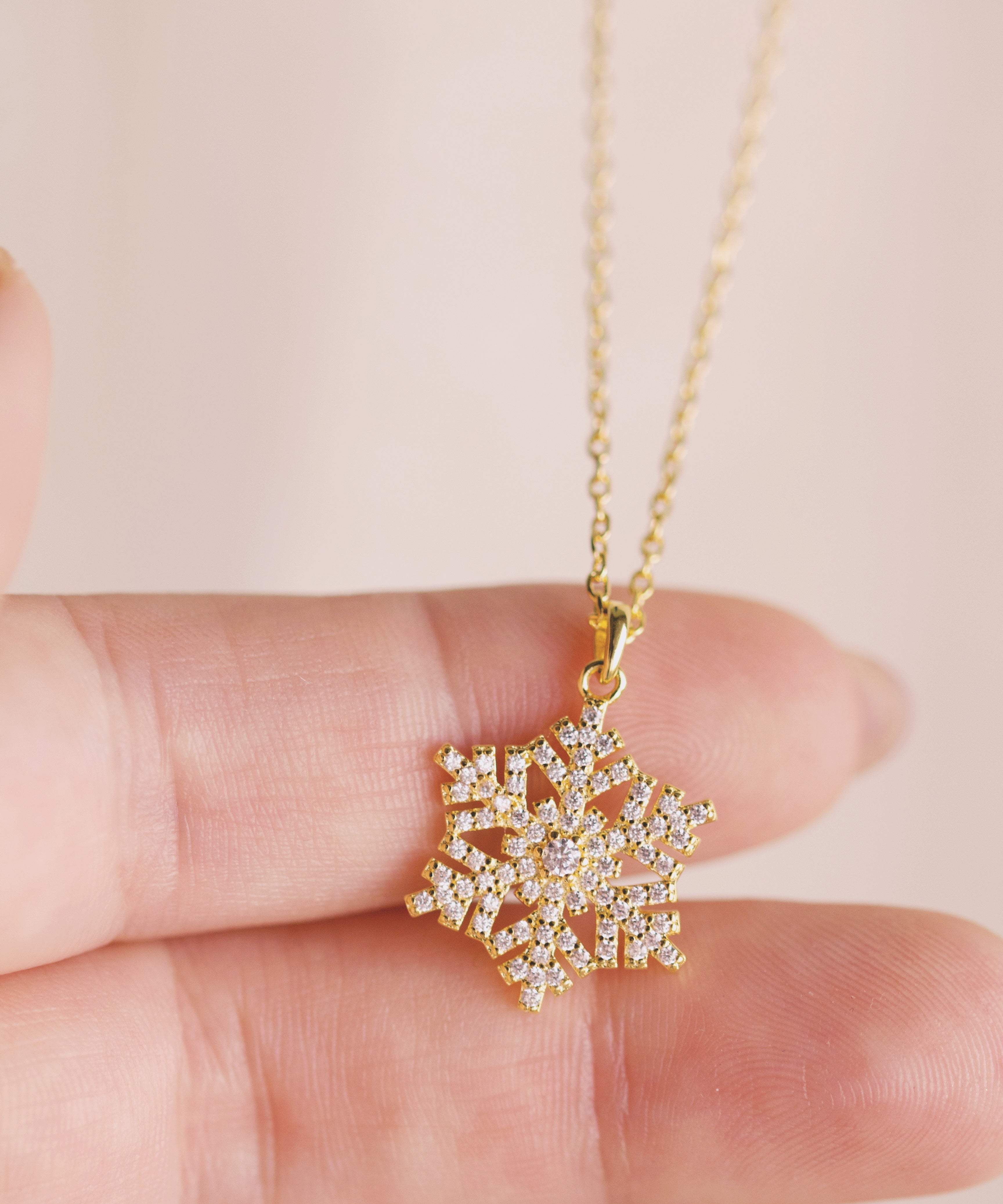 Gold snowflake pendant necklace held between fingers against a light background