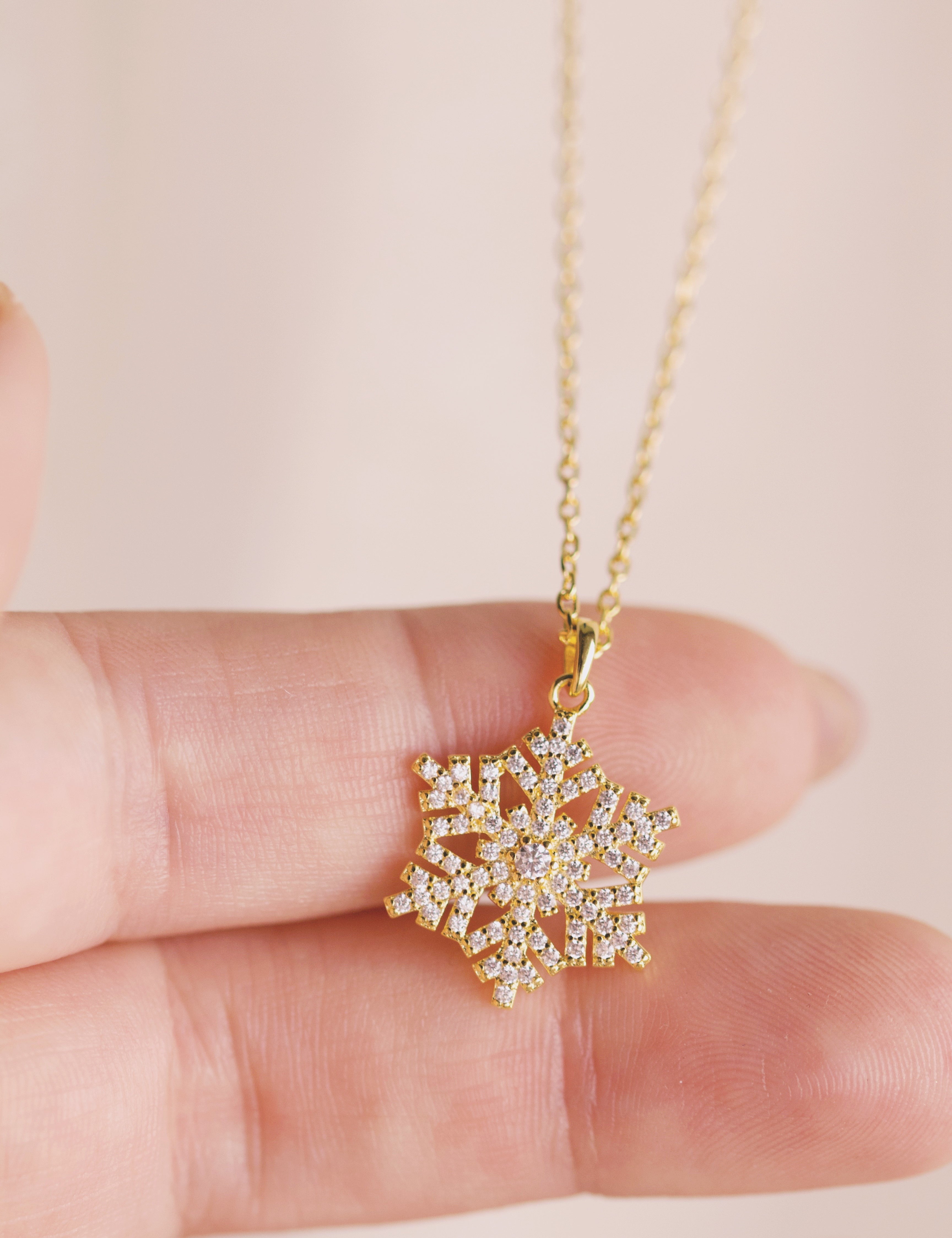 Gold snowflake pendant necklace held between fingers against a light background