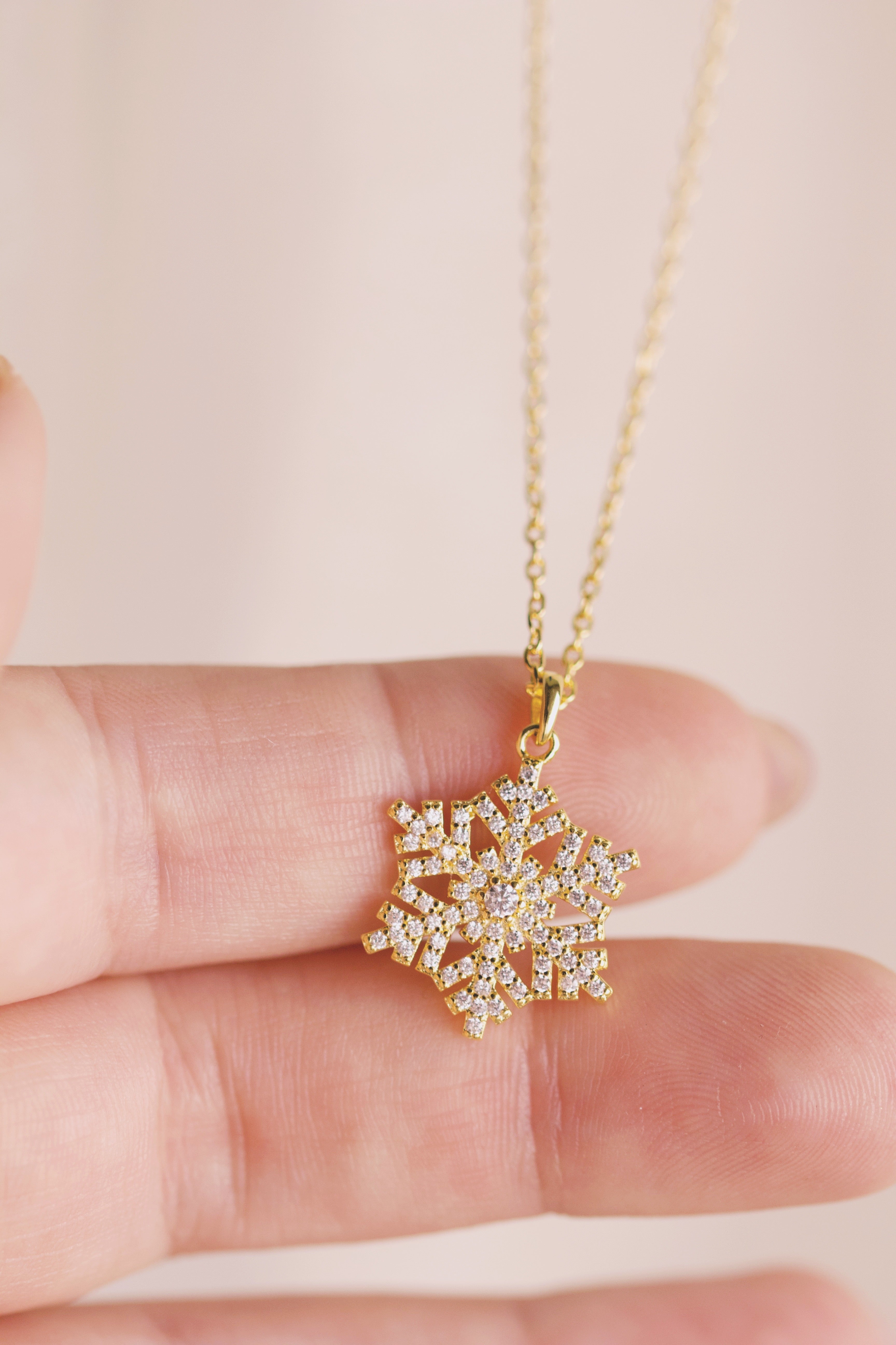 Gold snowflake pendant necklace held between fingers against a light background