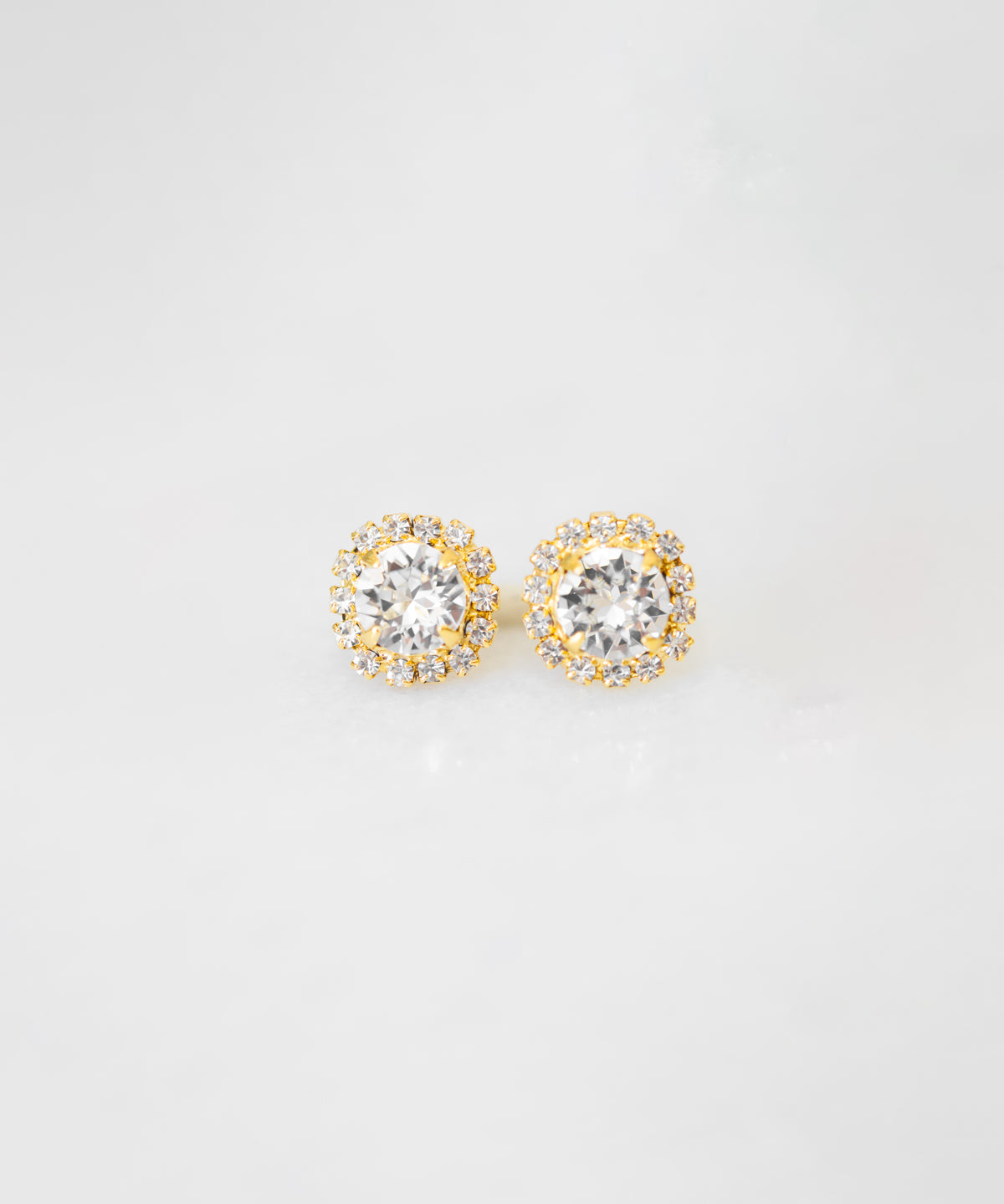 A pair of gold-colored stud earrings adorned with crystals, displayed against a white background.
