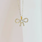 Gold bow-shaped pendant necklace on a light background