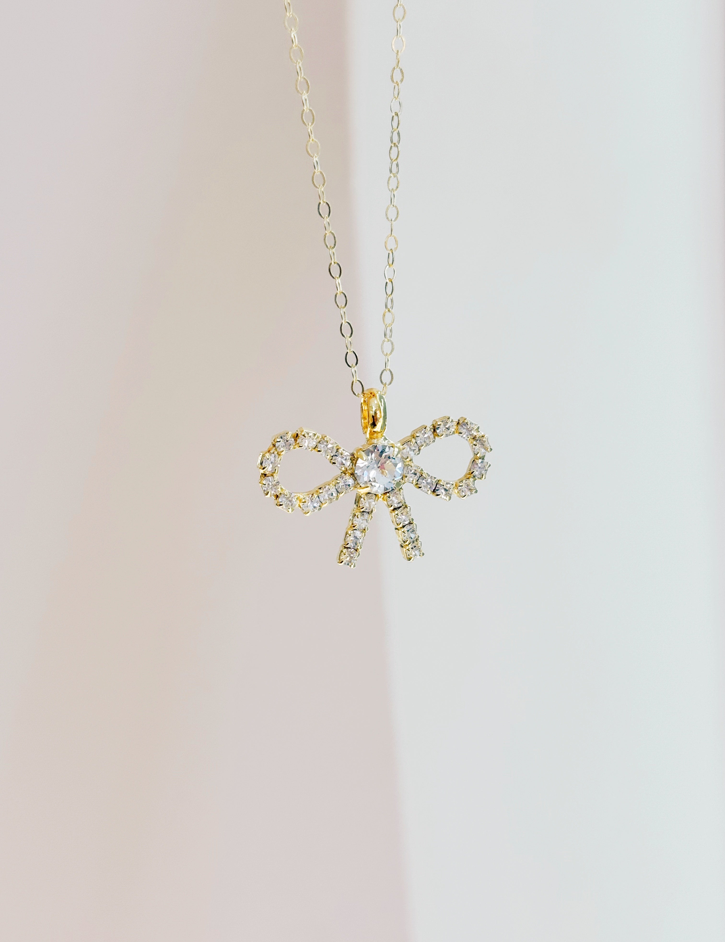 Gold bow-shaped pendant necklace on a light background