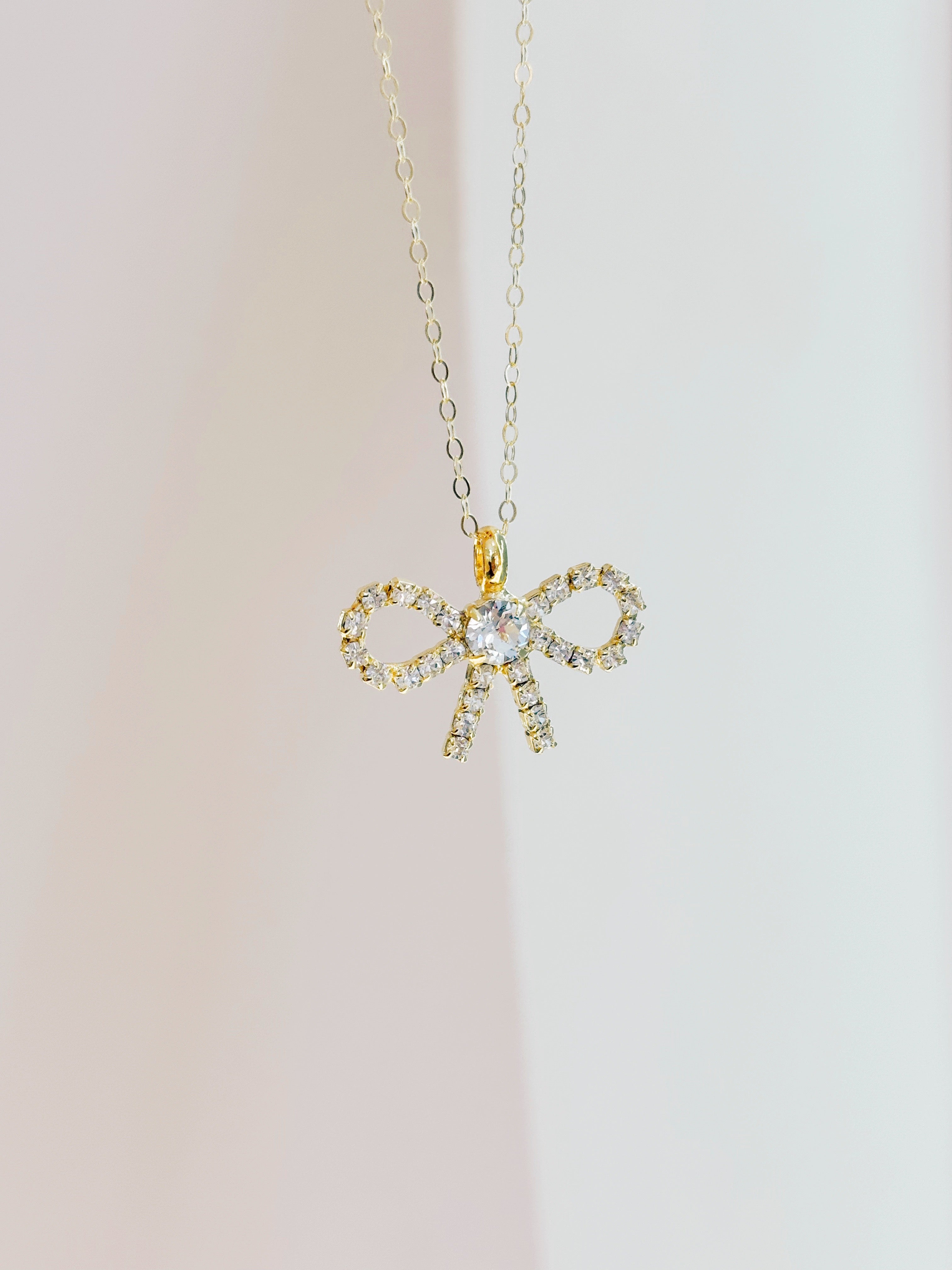 Gold bow-shaped pendant necklace on a light background
