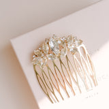 A gold-colored bridal hair comb with leaf and flower designs, adorned with Austrian crystals, displayed on a white background.