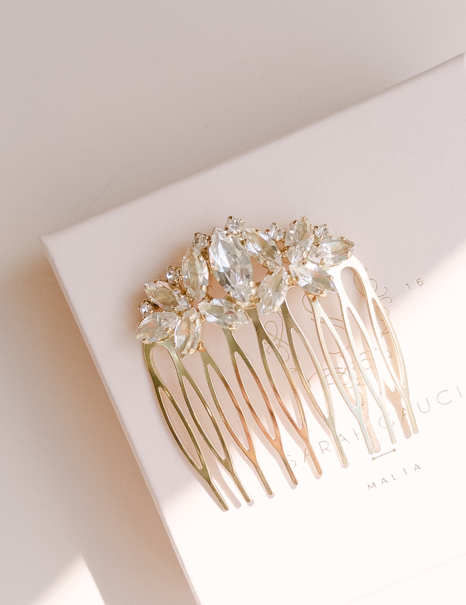 A gold-colored bridal hair comb with leaf and flower designs, adorned with Austrian crystals, displayed on a white background.