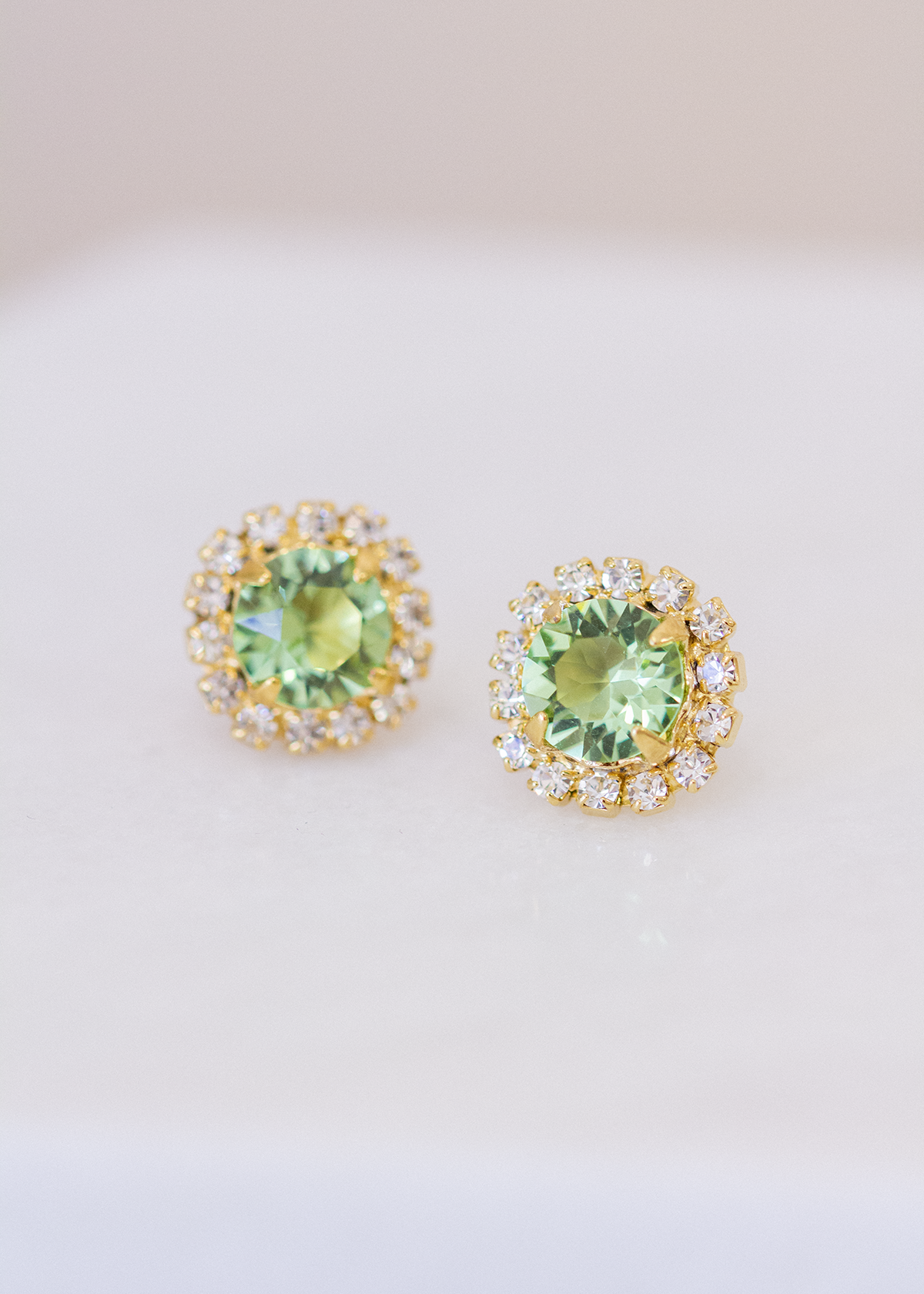 grand cassiopeia earrings in gold with surrounding halo of crystals and a peridot center crystal