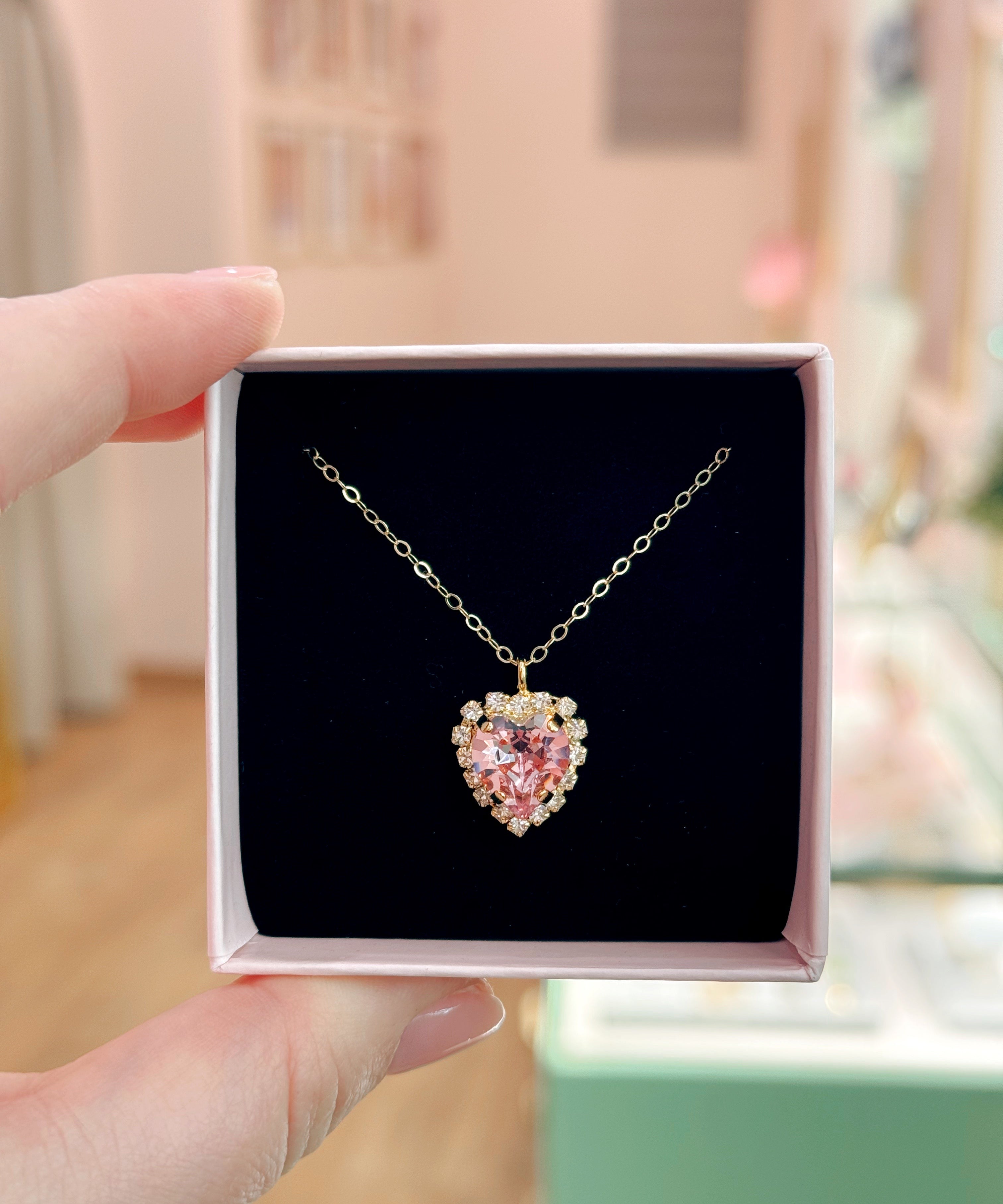 Heart-shaped necklace with pink gemstone in a box held by a hand