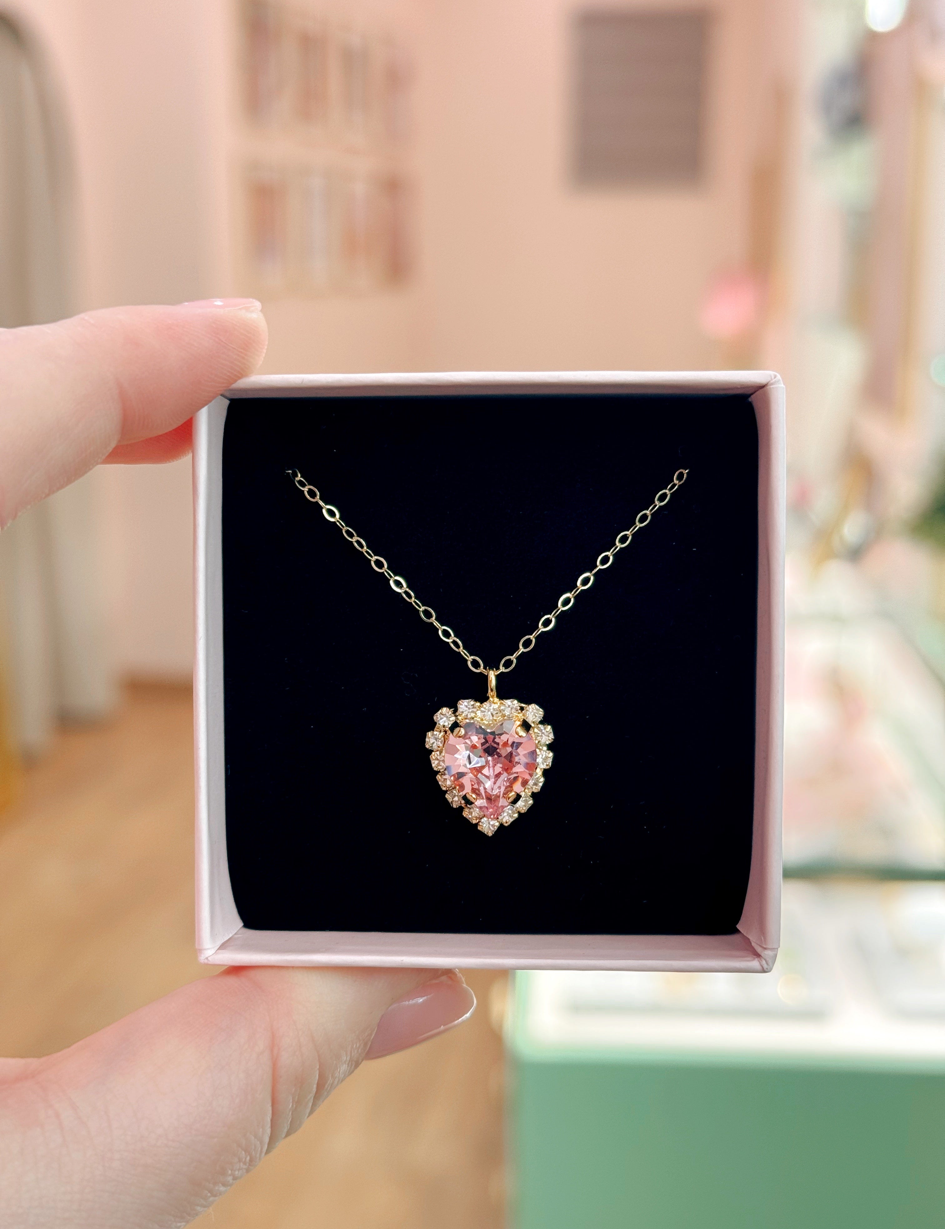 Heart-shaped necklace with pink gemstone in a box held by a hand