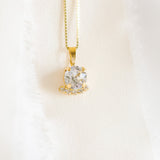 A gold-colored necklace with a round pendant adorned in crystals, displayed against a white fabric background.