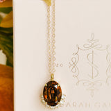 Gold necklace with a brown pendant on a white card with decorative text