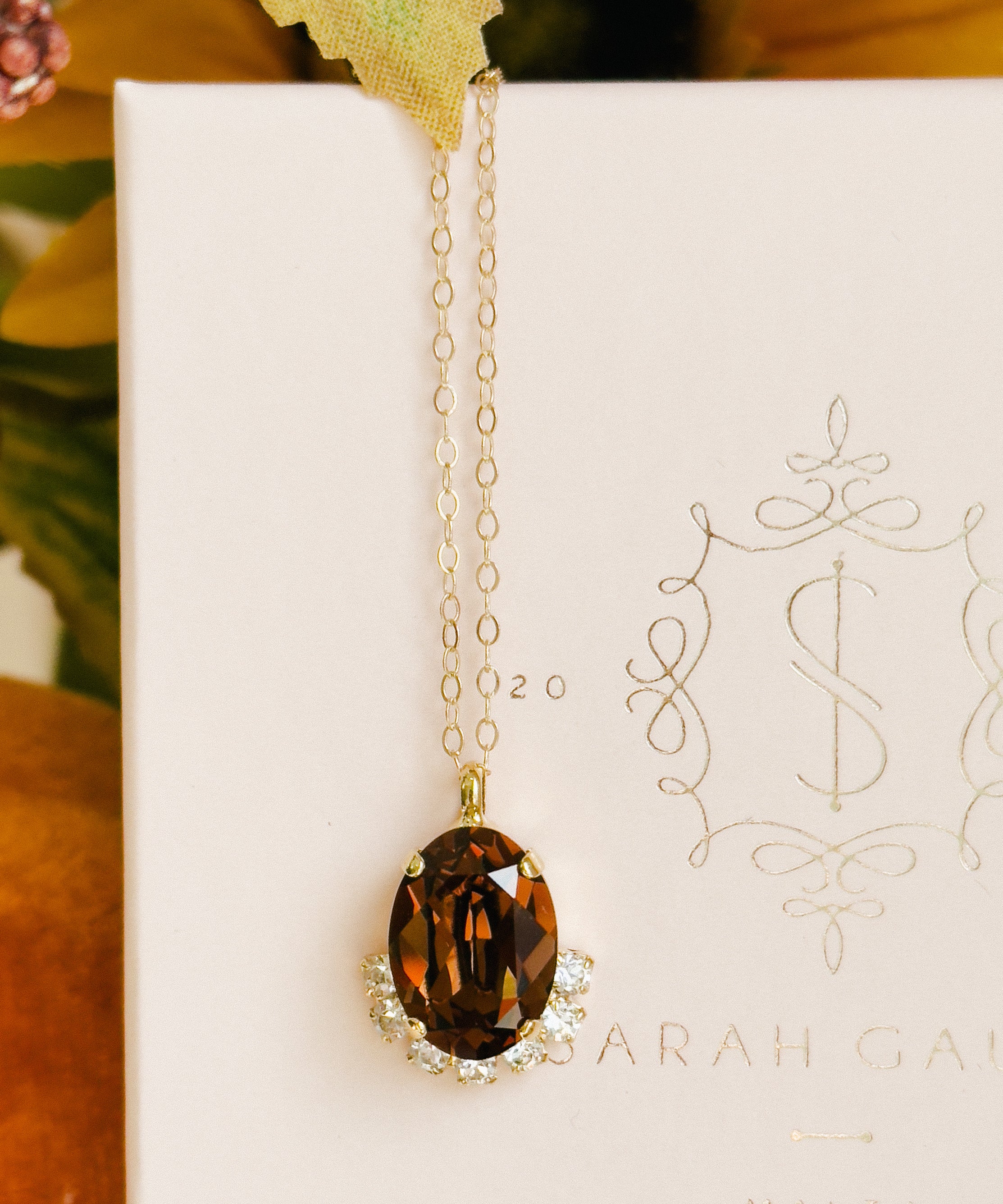 Gold necklace with a brown pendant on a white card with decorative text