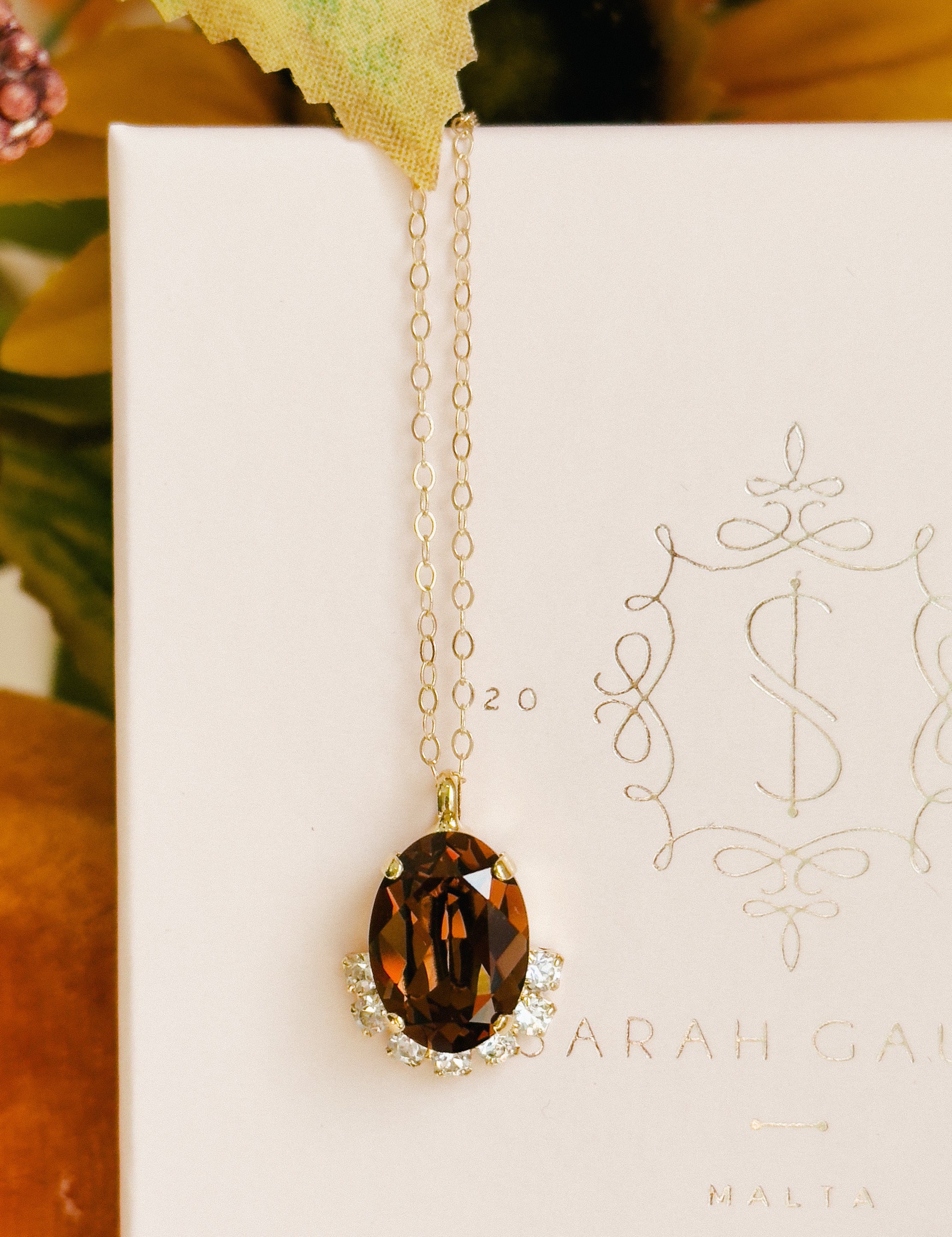 Gold necklace with a brown pendant on a white card with decorative text