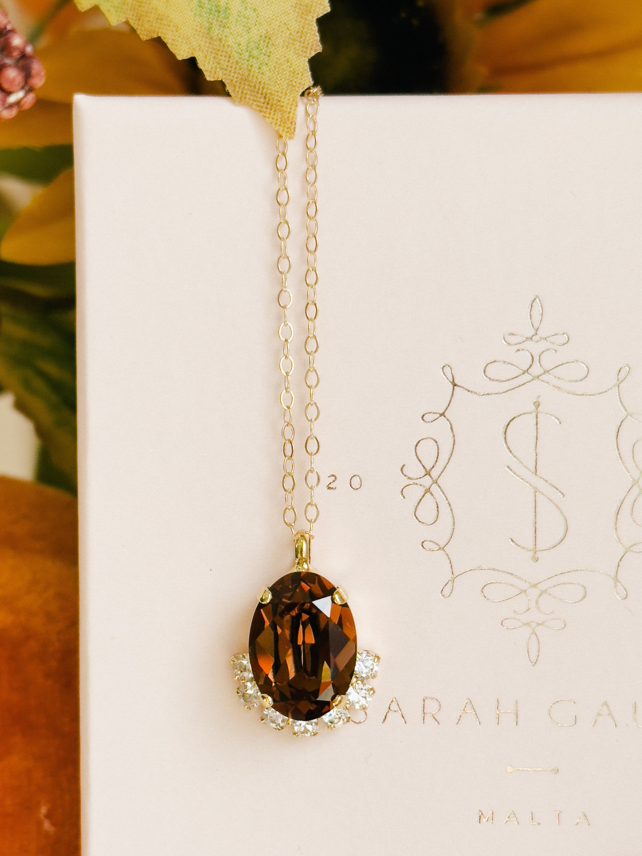 Gold necklace with a brown pendant on a white card with decorative text
