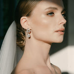 A woman wearing a white bridal veil and crystal stud drop earrings with a floral design by Sarah Gauci