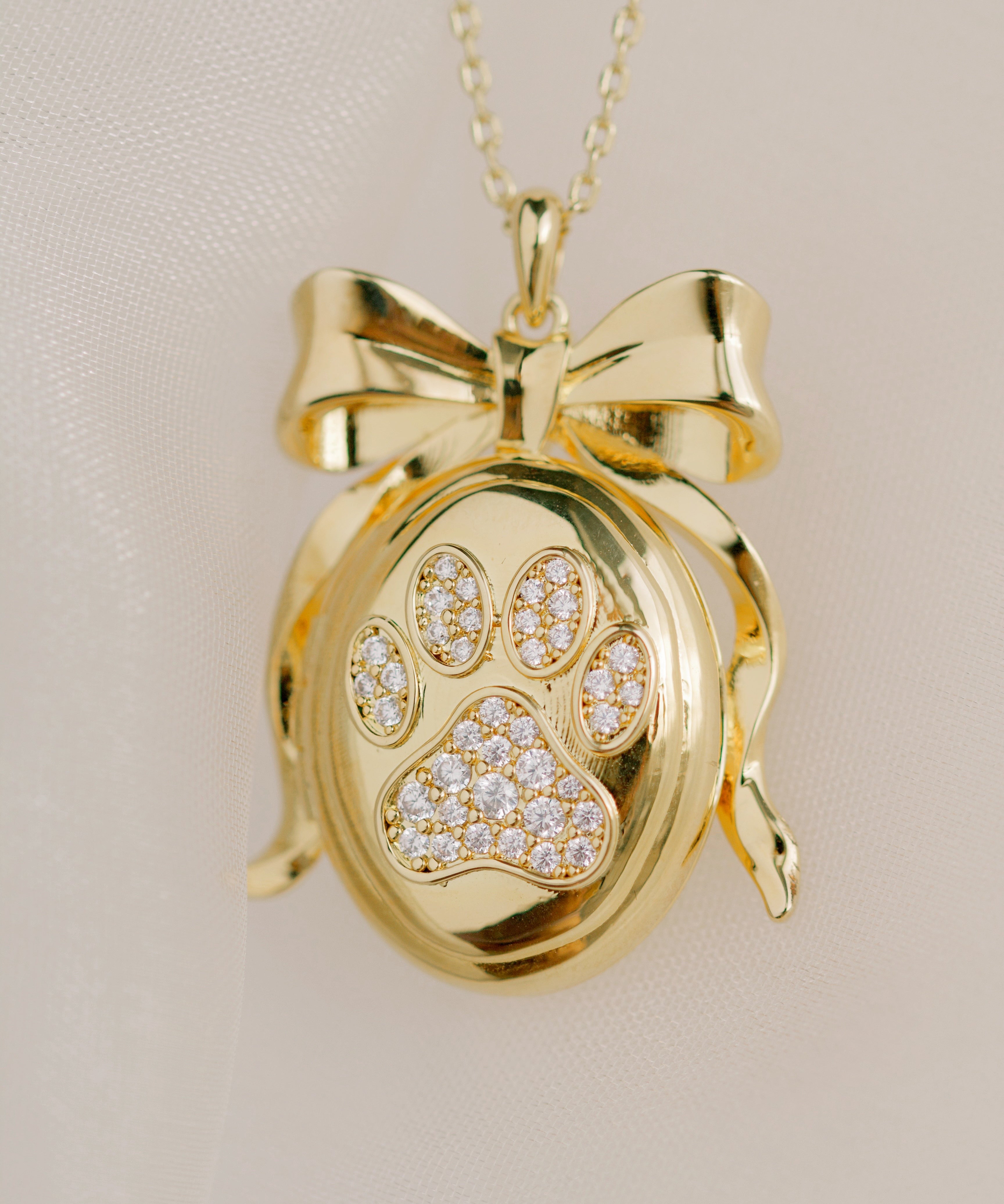 Gold pendant with paw print design on a beige background by Sarah Gauci Jewelry