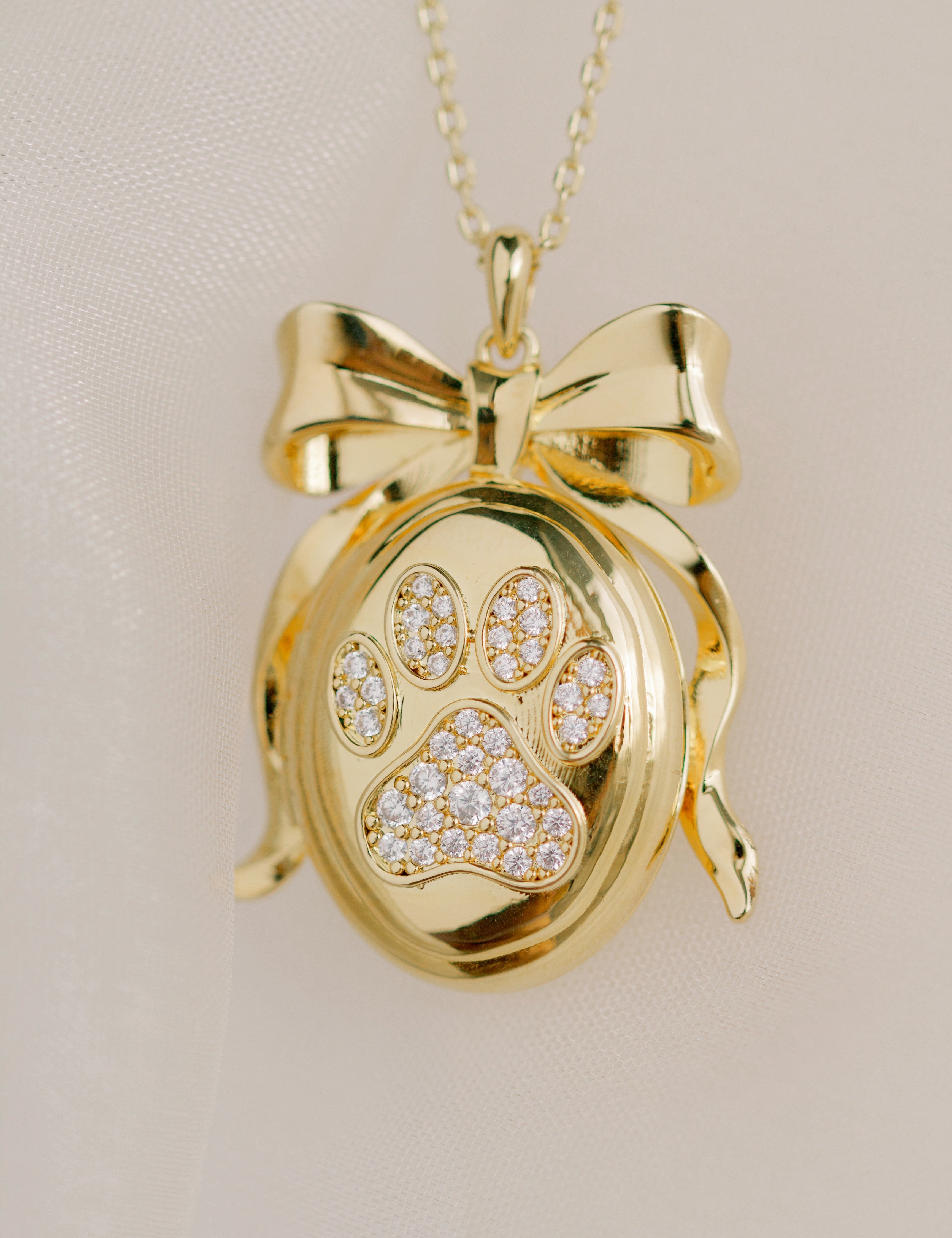 Gold pendant with paw print design on a beige background by Sarah Gauci Jewelry