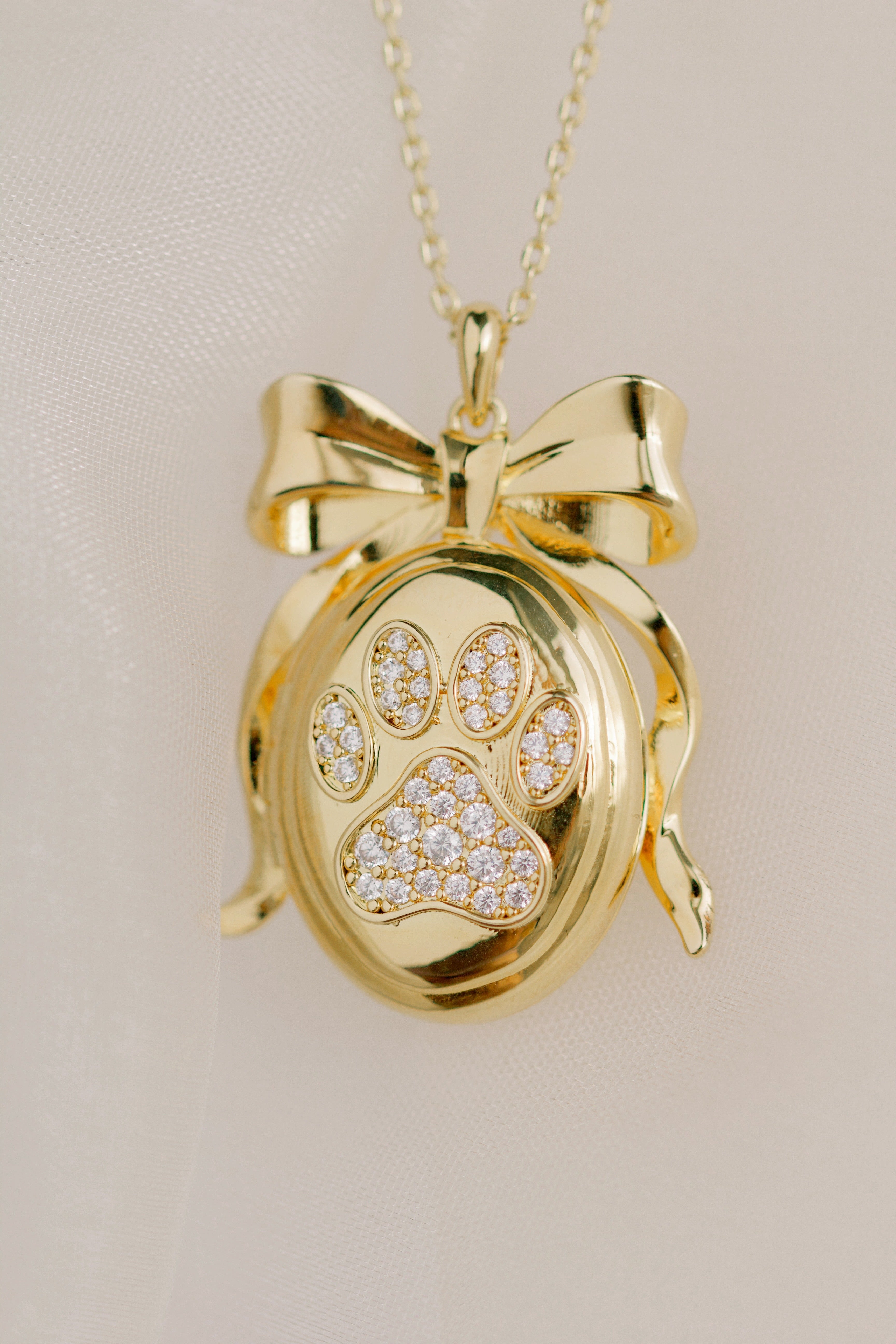 Gold pendant with paw print design on a beige background by Sarah Gauci Jewelry