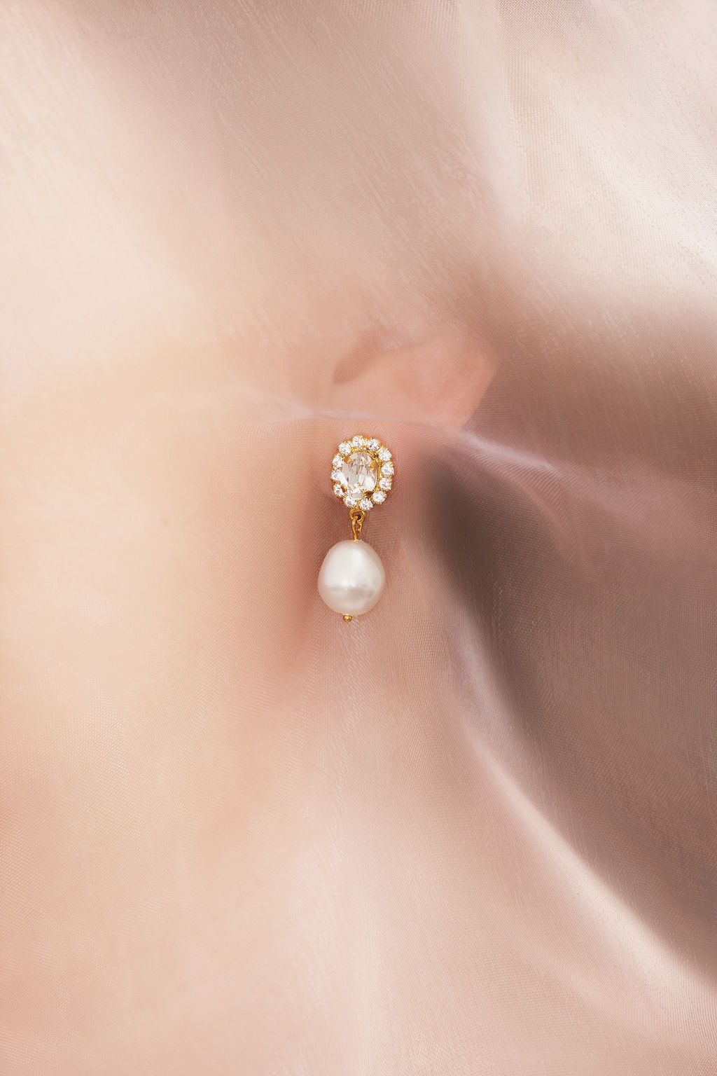 A close-up image of a woman's ear wearing a gold-plated earring with a baroque pearl and a sparkling crystal atop.