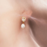 A close-up image of a woman's ear wearing a gold-plated earring with a baroque pearl and a sparkling crystal atop.