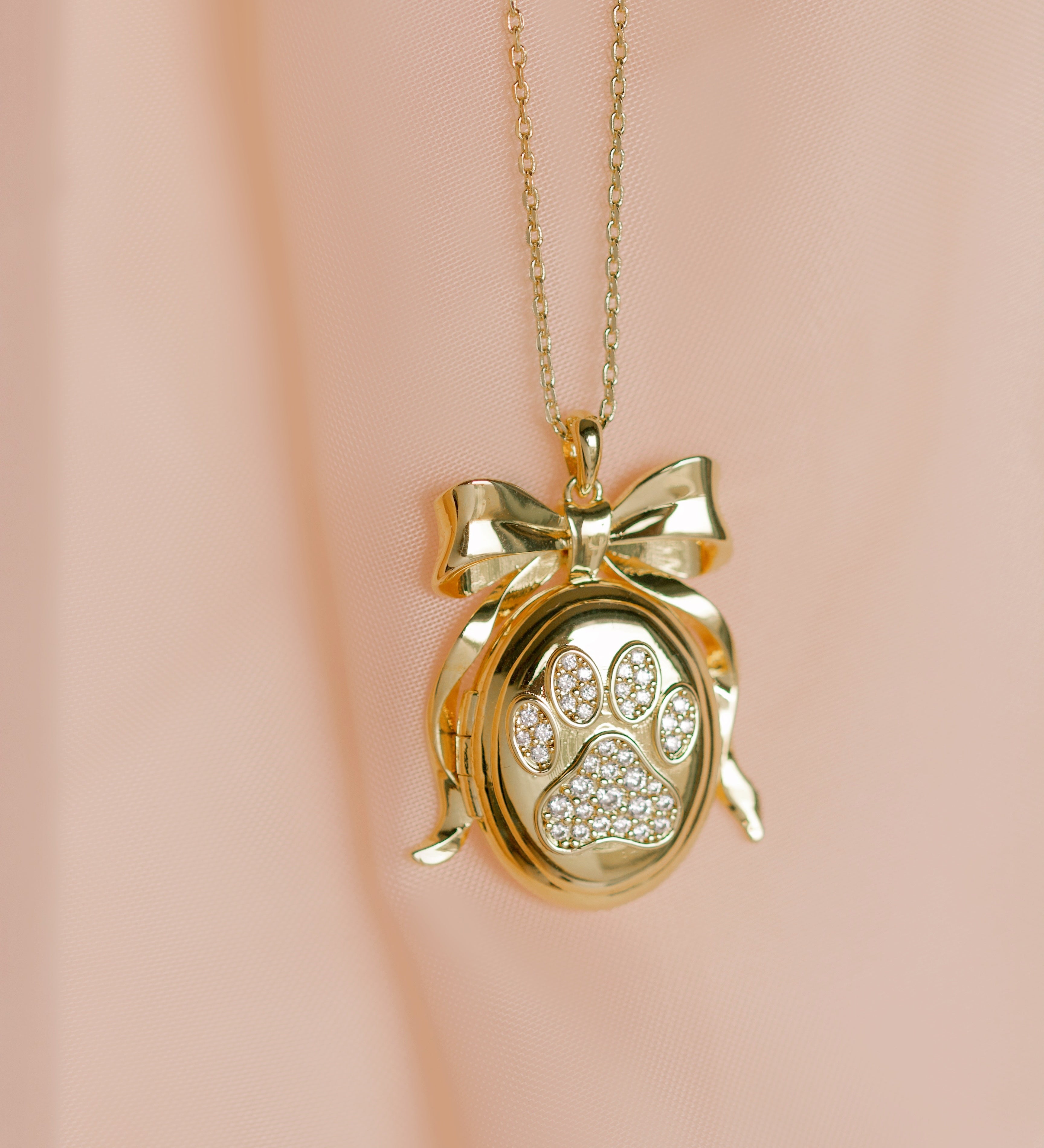 Gold necklace with a paw print locket on a pink background