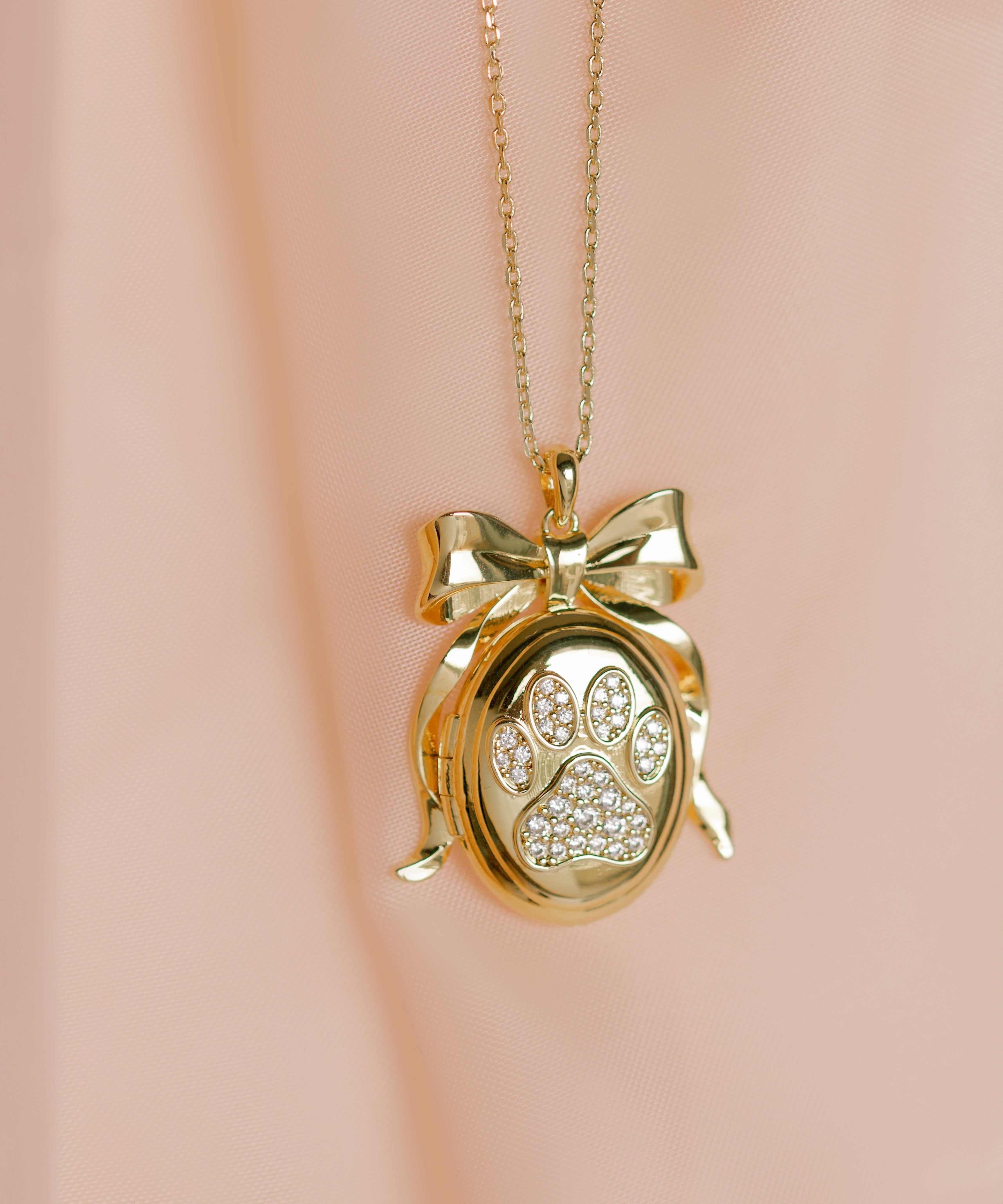 Gold necklace with a paw print locket on a pink background