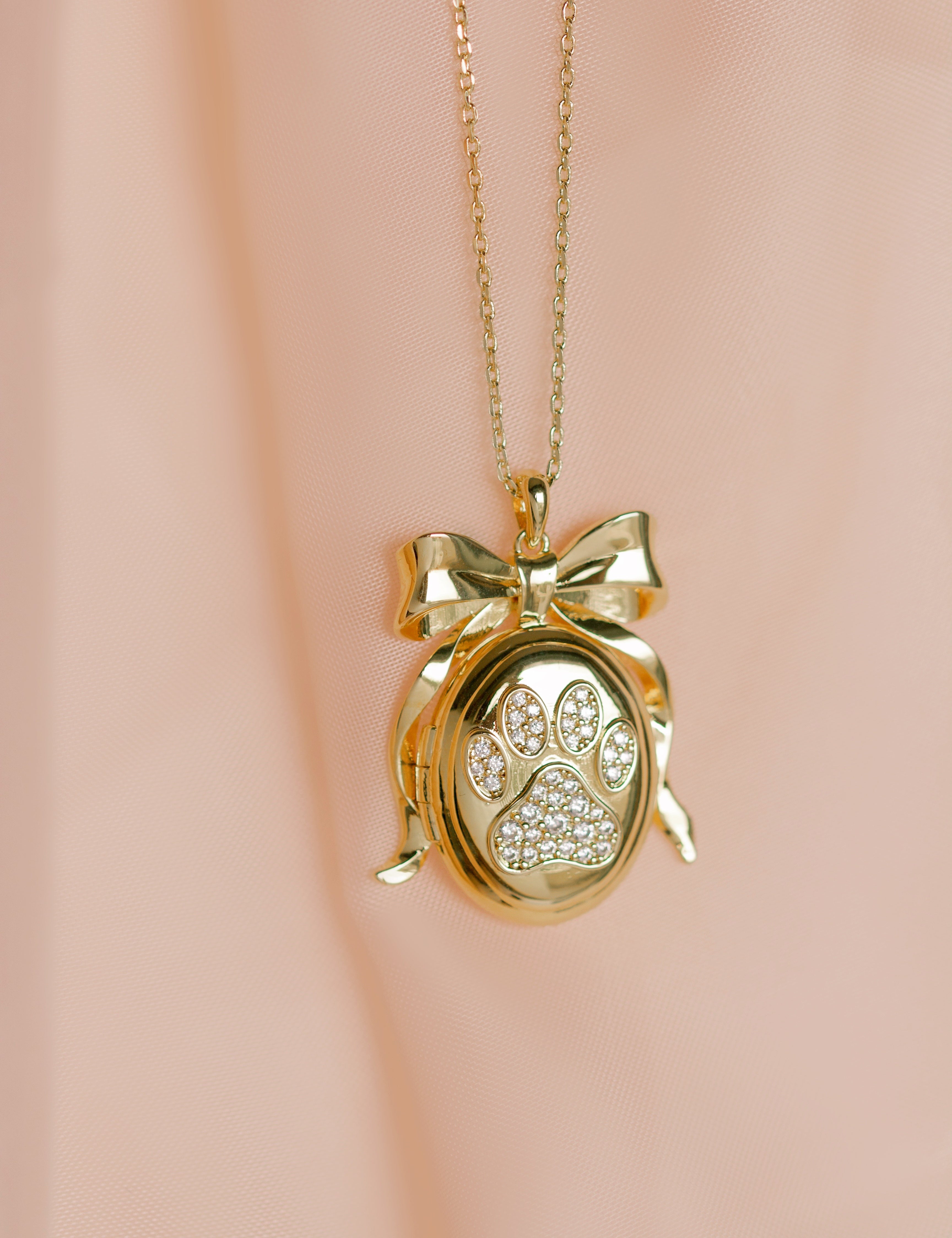 Gold necklace with a paw print locket on a pink background