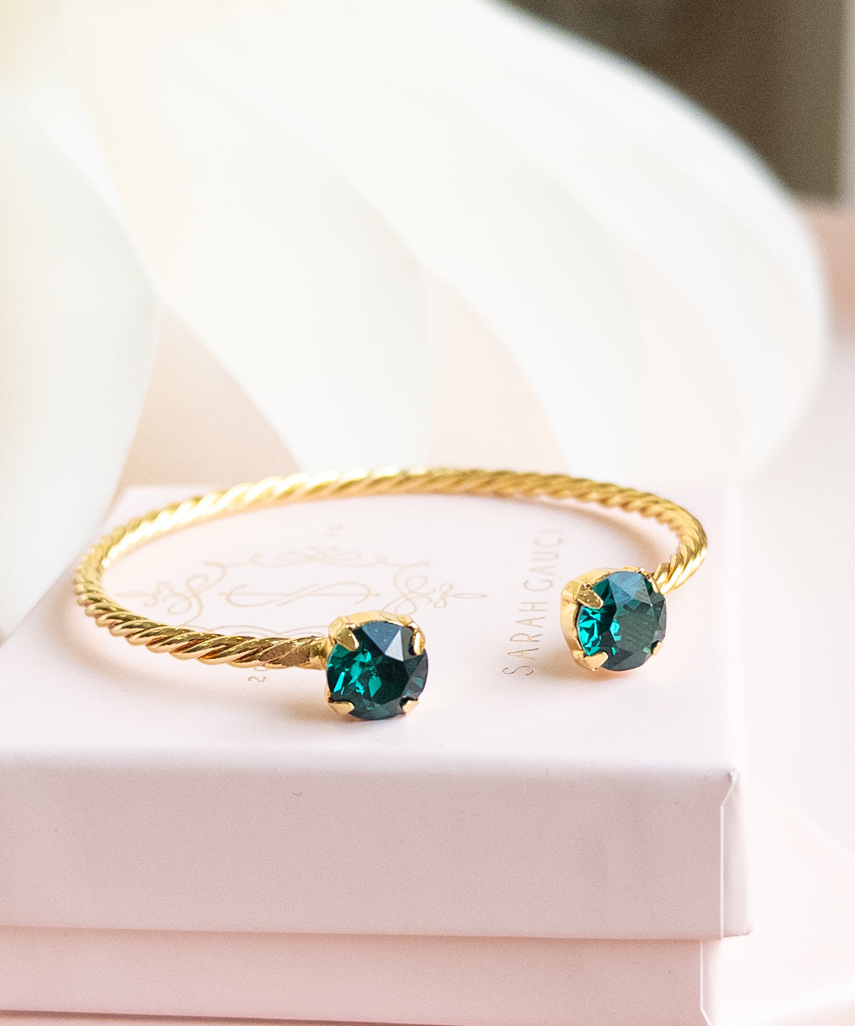 Gold bracelet with green gemstones on a white surface