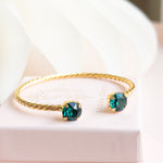 Gold bracelet with green gemstones on a white surface