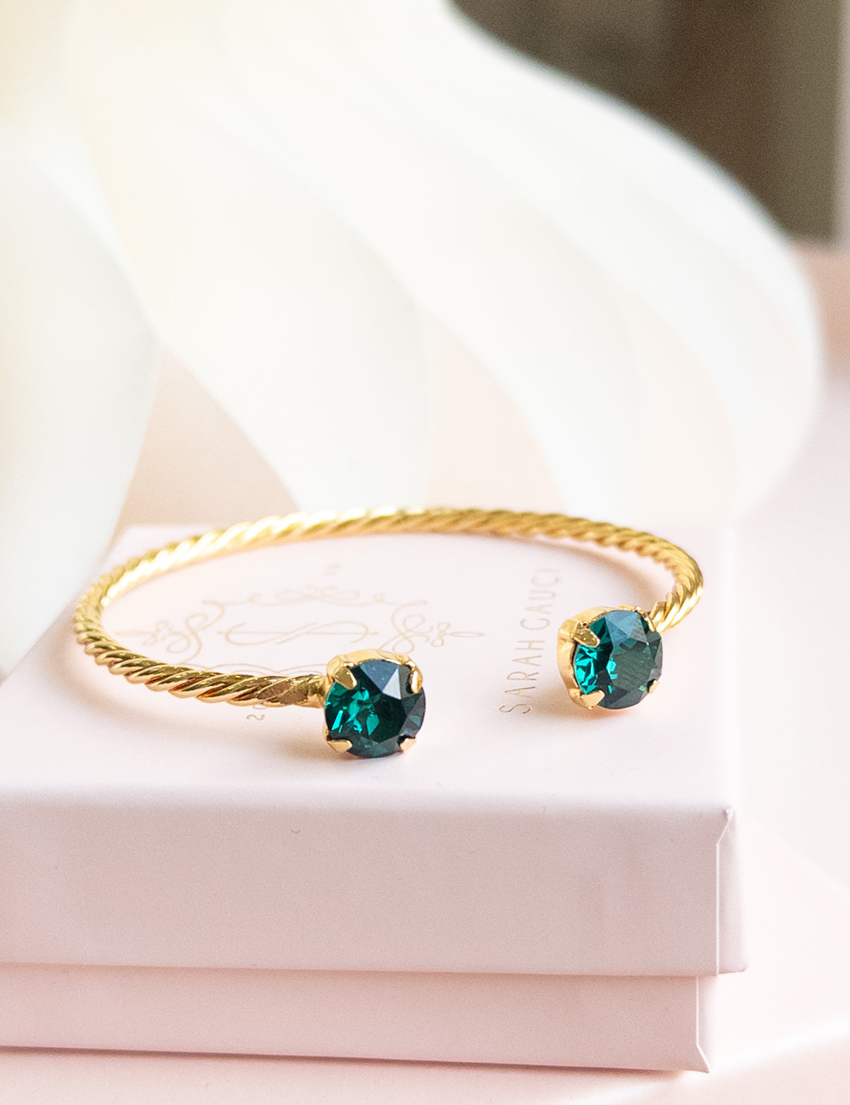 Gold bracelet with green gemstones on a white surface