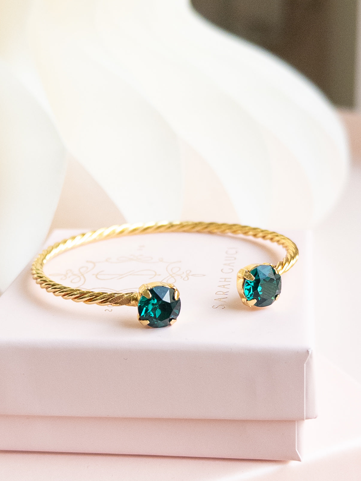 Gold bracelet with green gemstones on a white surface