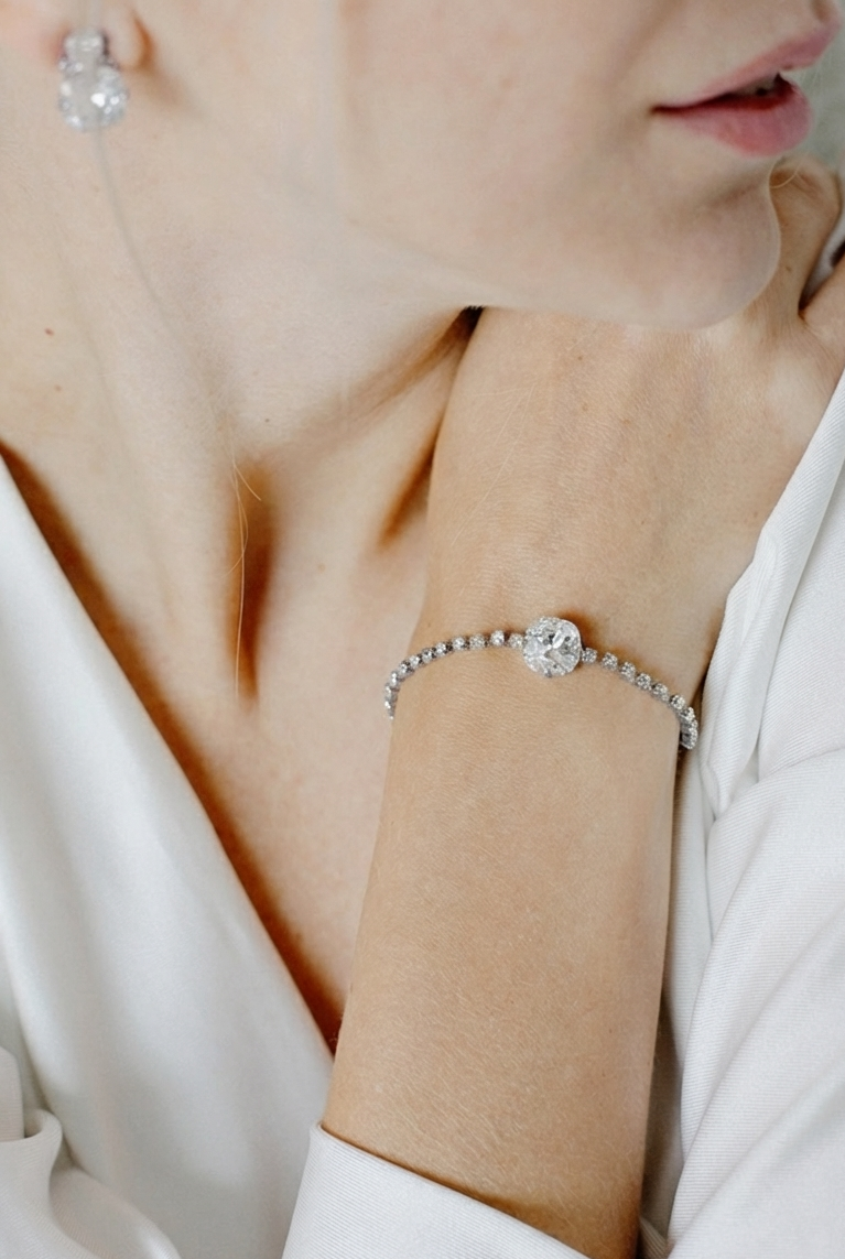 Close-up of a person wearing a silver bracelet with a clear stone on a white background.