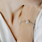 Close-up of a person wearing a silver bracelet with a clear stone on a white background.