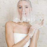 A Bride wearing a white wedding dress, veil, and gloves against a neutral background