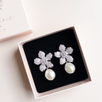 A pair of floral design pearl bridal earrings with a silver finish and white pearl drops, by Sarah Gauci
