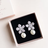 A pair of floral design pearl bridal earrings with a silver finish and white pearl drops, by Sarah Gauci