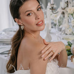 A bride wearing elegant white attire with long sleeves, featuring the Lettie Bridal Stud Swarovski Crysal Earrings with cascading crystals.